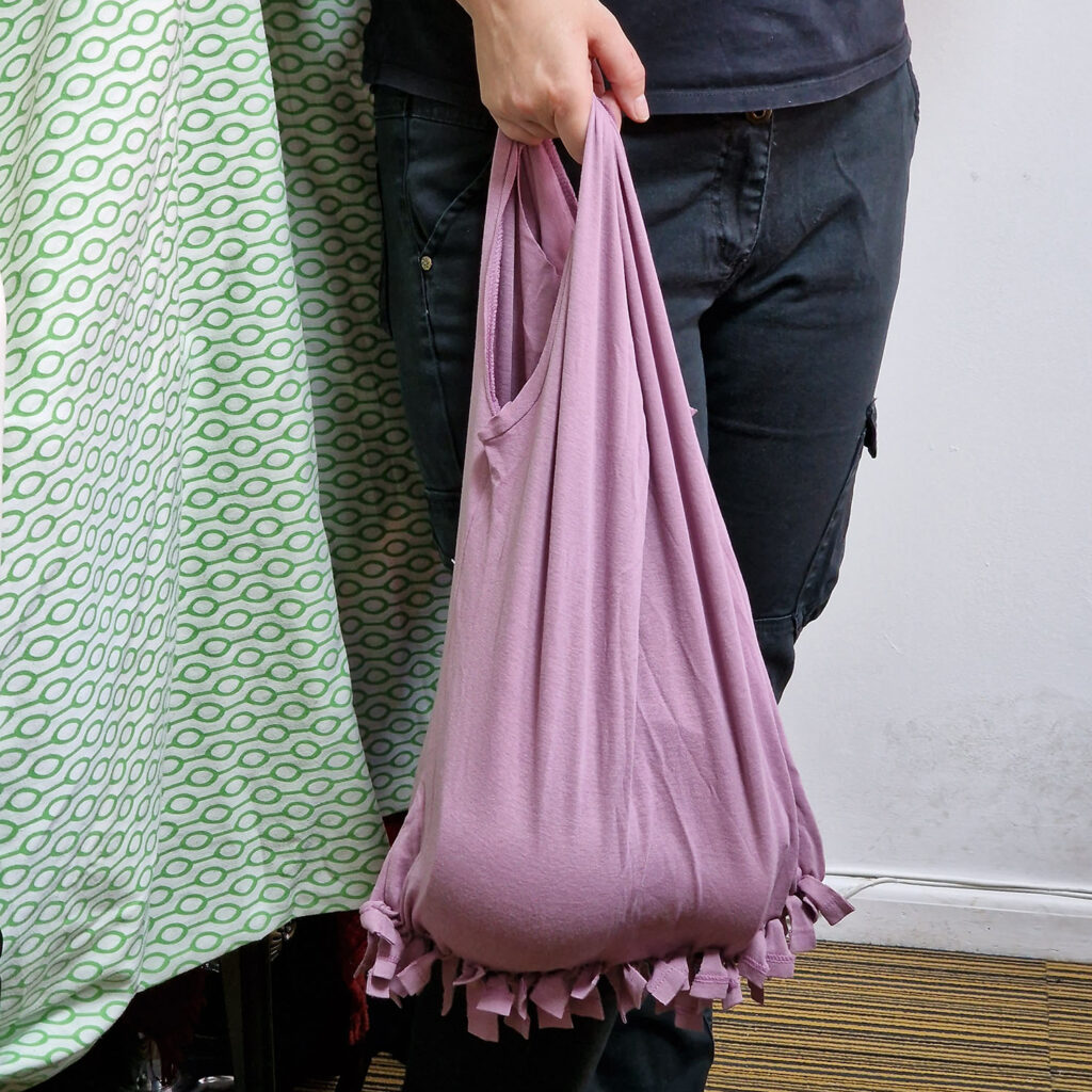 a hand holding a handbag made from the t-shirt. The handles are the sleeve holes and the bottom is strips tied together.